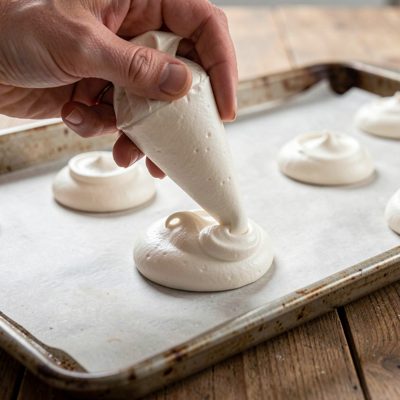 a hand piping meringue onto a baking sheet