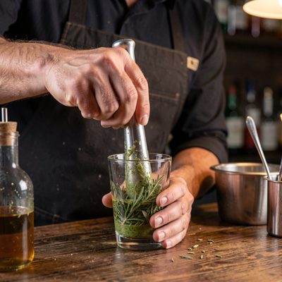 a mixologist muddling herbs in a glass