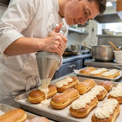 a pastry chef piping cream into eclairs