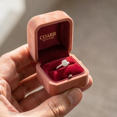 a hand holding an engagement ring box open