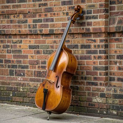 a double bass leaning against a brick wall