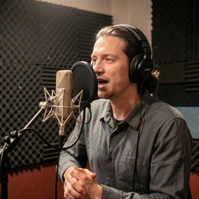 a singer songwriter recording vocals in a booth