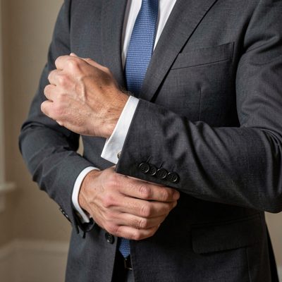 an adult man in a tailored suit adjusting his cuff