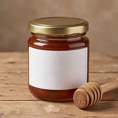 a honey jar with a blank white label and a wooden dipper beside it