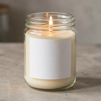 a candle in a glass jar with a blank unprinted white label