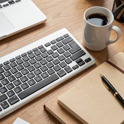 a keyboard with a mug and notebook beside